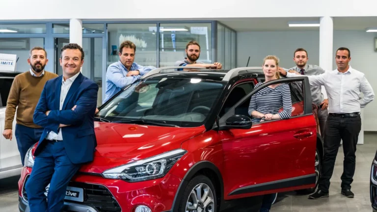 Équipe commerciale Hyundai posant devant un véhicule rouge